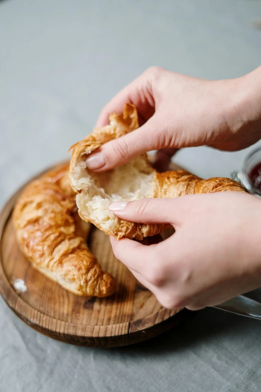 a person holding a pastry on top of a wooden plate, by Tom Bonson, trending on unsplash, melting cheese, dog eating croissants in paris, cooking, on grey background