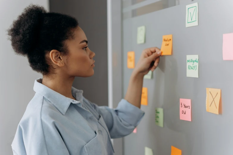 a woman standing in front of a wall covered in post it notes, trending on pexels, studying in a brightly lit room, profile image, with labels and notes, medium close up shot