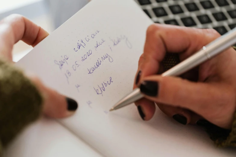 a person holding a pen and writing on a piece of paper, by Julia Pishtar, notebook, eal, up close image