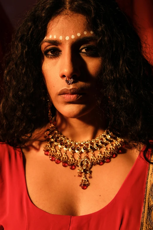 a woman in a red dress posing for a picture, an album cover, inspired by Raja Ravi Varma, renaissance, wearing gold detailed choker, cinematic and dramatic red light, close up half body shot, elaborate oled jewelry