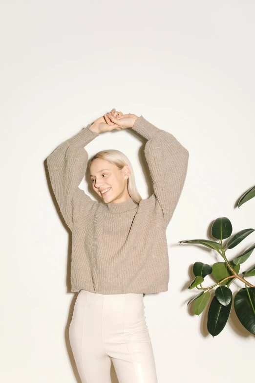 a woman standing in front of a potted plant, by Carey Morris, trending on unsplash, he is wearing a brown sweater, light grey, voluminous sleeves, kirsi salonen