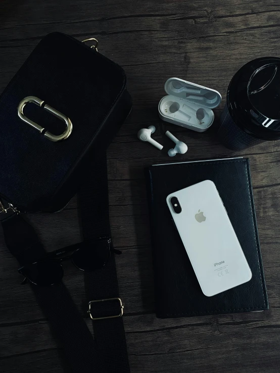 a black purse sitting on top of a wooden table, by Niko Henrichon, trending on pexels, happening, airpods, white gold skin, dark academia aesthetic, 4 k hd wallpapear