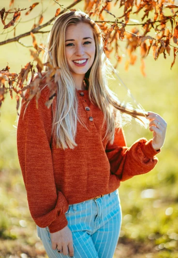 a woman standing under a tree in a field, by Robbie Trevino, trending on pexels, renaissance, long orange sweatshirt, smiling fashion model, cropped wide sleeve, blonde