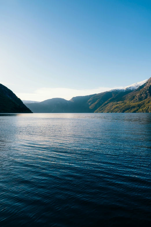 a body of water with mountains in the background, fjords, low sun, clear blue skies, null