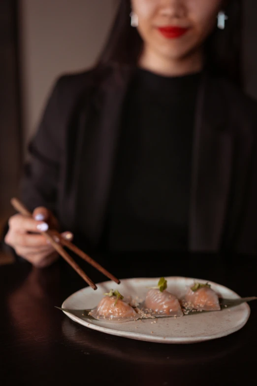 a woman sitting at a table with a plate of food and chopsticks, gushy gills and blush, moody iconic scene, grey, sparkling