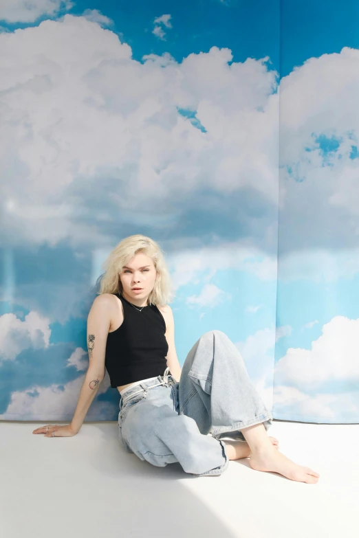 a woman sitting on top of a white floor, an album cover, by Gee Vaucher, tattoos of cumulus clouds, anya taylor - joy, cyan photographic backdrop, jeans and t shirt