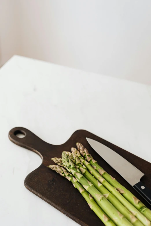 a cutting board with a bunch of asparagus on it, unsplash, clean minimalist design, multiple stories, indoor picture, holding knife