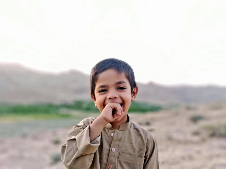 a little boy that is standing in the dirt, by Riza Abbasi, pexels contest winner, hurufiyya, small beard, in a scenic background, charming expression gesicht, slightly pixelated