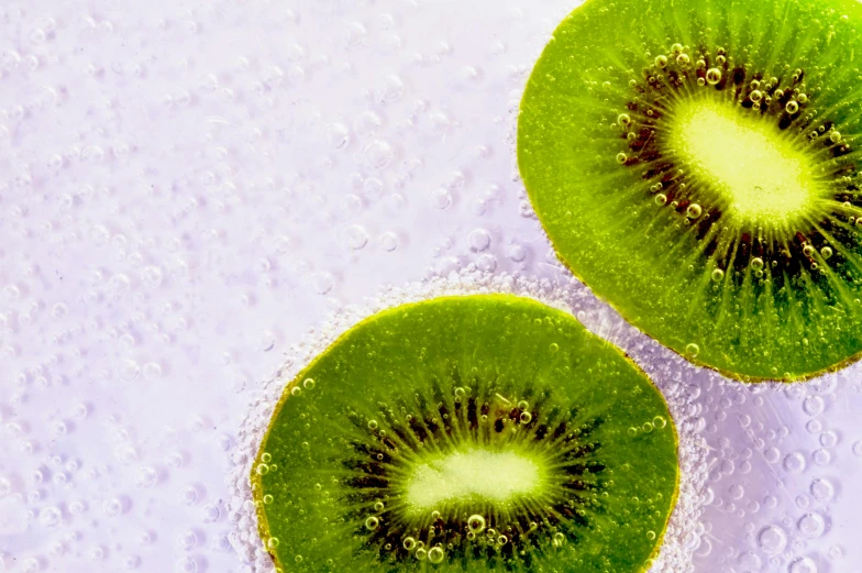 two slices of kiwi sitting next to each other, by Winona Nelson, trending on pexels, hurufiyya, bubble bath, purple and green, overexposed photograph, lightweight