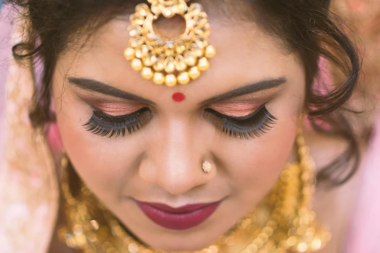 a close up of a woman wearing gold jewelry, trending on pixabay, hurufiyya, lashes, assamese aesthetic, a high angle shot, [ realistic photography ]