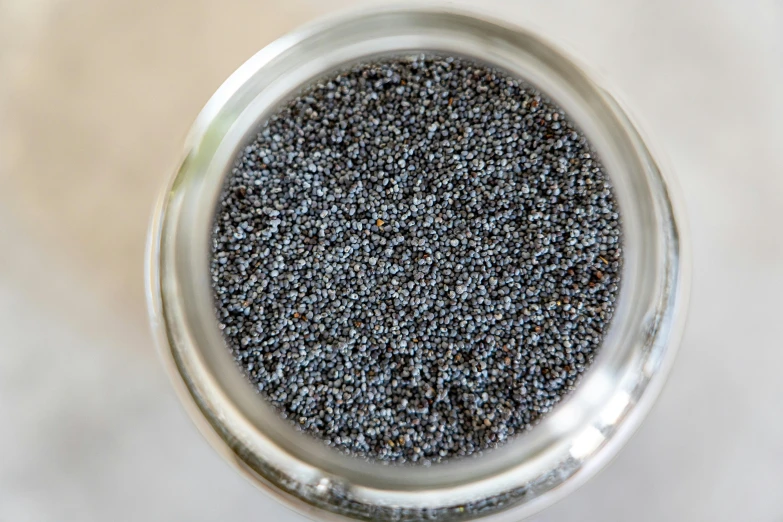 a jar filled with black seeds sitting on top of a table, a stipple, gun metal grey, 3 mm, birdseye view, sand