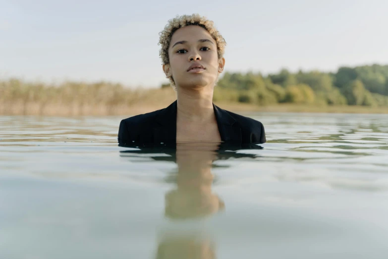 a woman standing in the middle of a body of water, short blonde afro, girl in suit, gen z, portait image