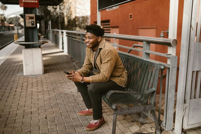 a man sitting on a bench at a train station, by Marshall Arisman, pexels contest winner, looking happy, jaylen brown, who is a male android, he is wearing a brown sweater