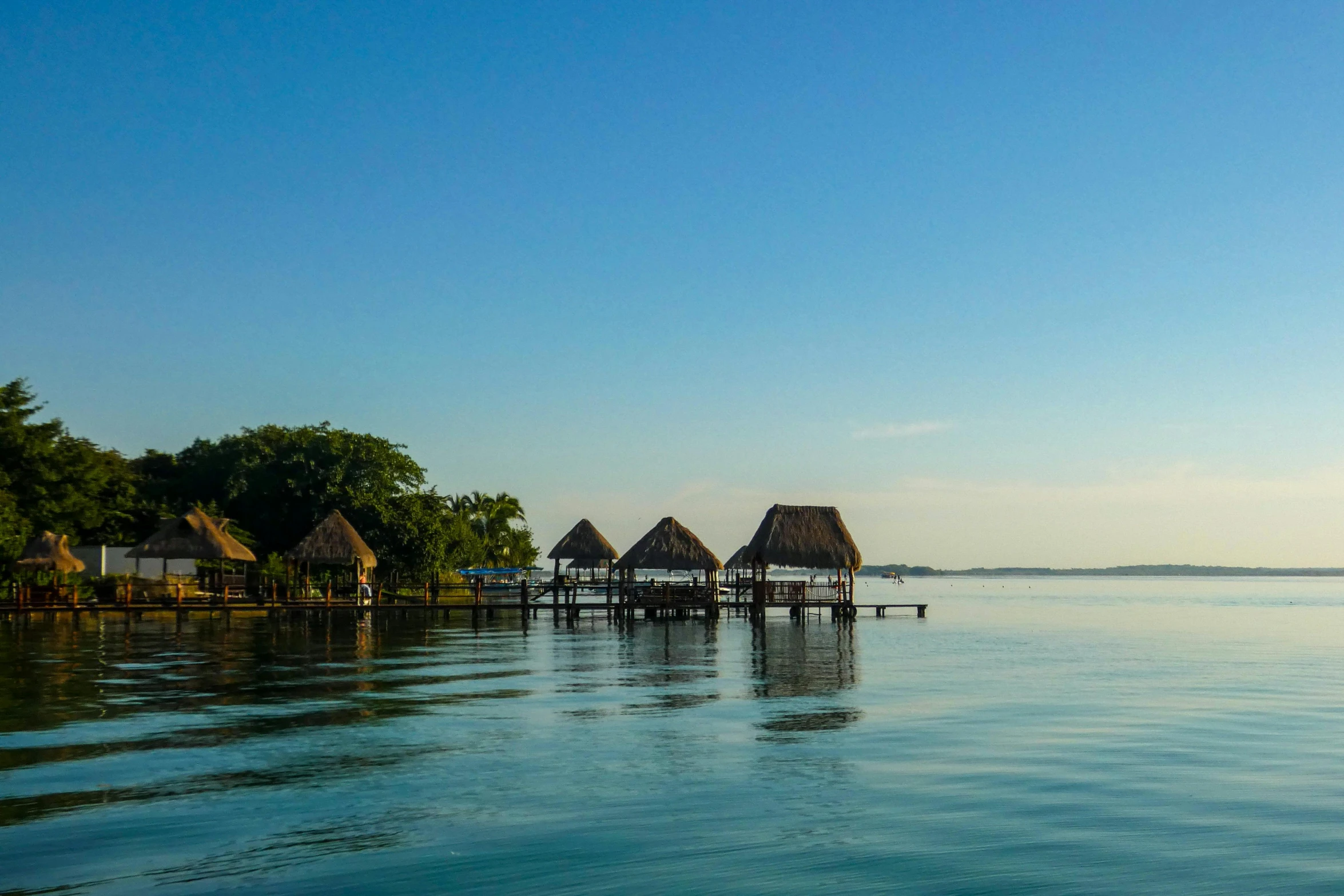 a group of huts sitting on top of a body of water, light blue water, afternoon, skies, blue water