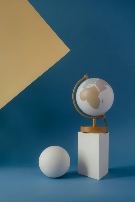 a globe sitting on top of a table next to a ball, light grey blue and golden, medium poly, explorer, paul barson