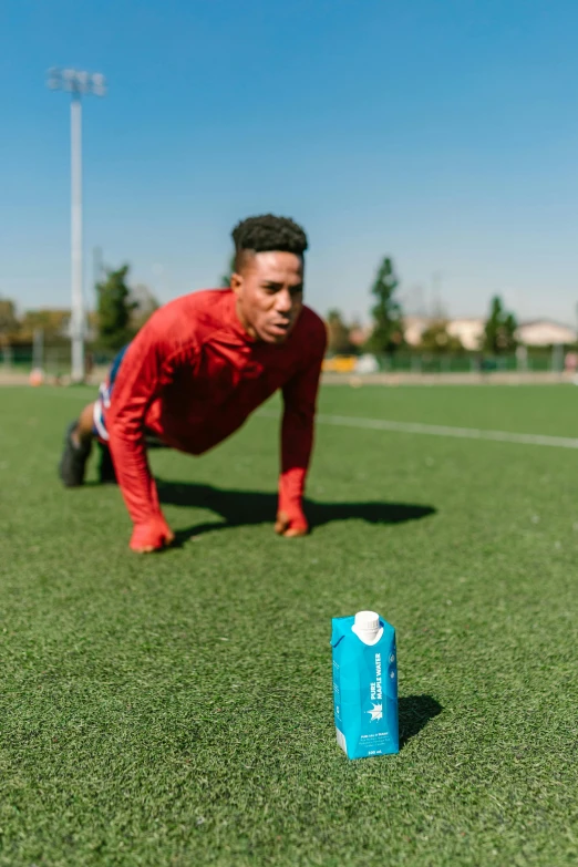 a man doing push ups on a soccer field, holding a bottle of arak, teal energy, taken on iphone 14 pro, square