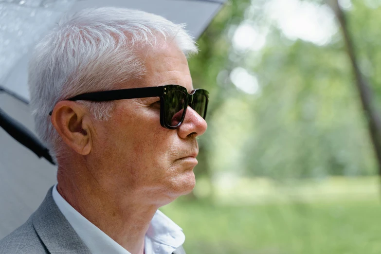 a man in a suit and sunglasses holding an umbrella, inspired by David Chipperfield, profile image, white haired, garden behind the glasses, profile close-up view