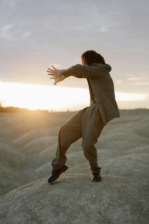 a man standing on top of a large rock, an album cover, unsplash, renaissance, karate pose, during golden hour, lois greenfield, wearing a track suit