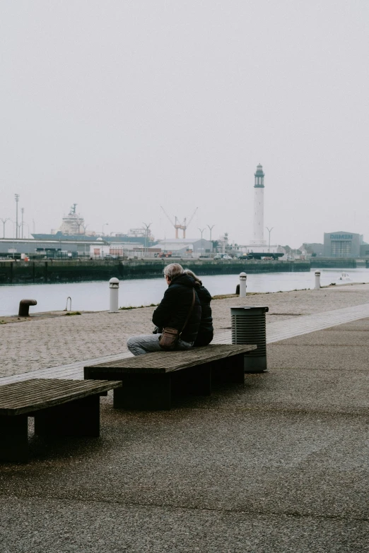 a man sitting on a bench next to a body of water, pexels contest winner, visual art, harbor, under a gray foggy sky, older male, lo fi