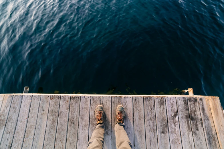 a person standing on a dock next to a body of water, pexels contest winner, photorealism, feet on the ground, looking down from above, looking off into the distance, guide
