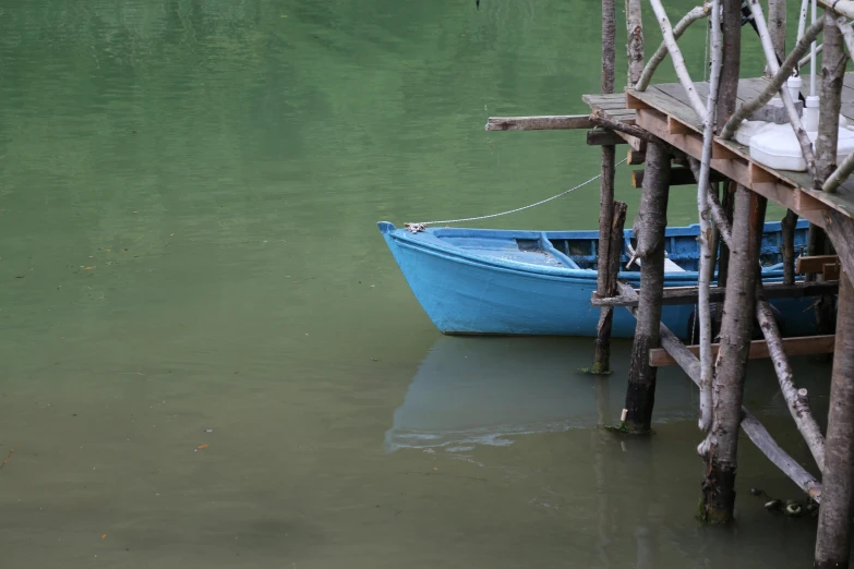 a blue boat sitting on top of a body of water, by Elsa Bleda, pexels contest winner, hurufiyya, muted green, a wooden, grey, small dock