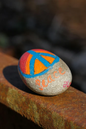 a rock with a peace sign painted on it, by Jessie Algie, orange and blue, slide show, exterior shot, multi colour