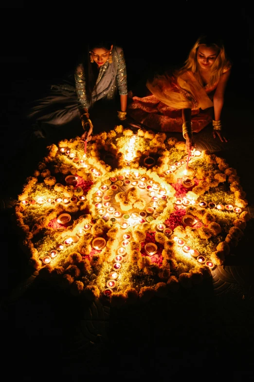a group of people sitting around a fire pit, an album cover, by Dan Content, pexels contest winner, process art, hindu ornaments, glowing lights!! intricate, light casting onto the ground, petals