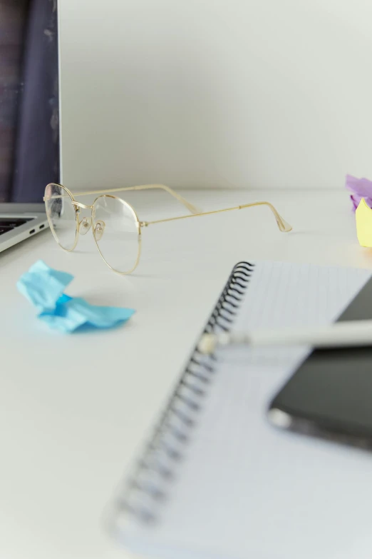 a laptop computer sitting on top of a white desk, half-frame square glasses, belongings strewn about, detail shot, pastel'