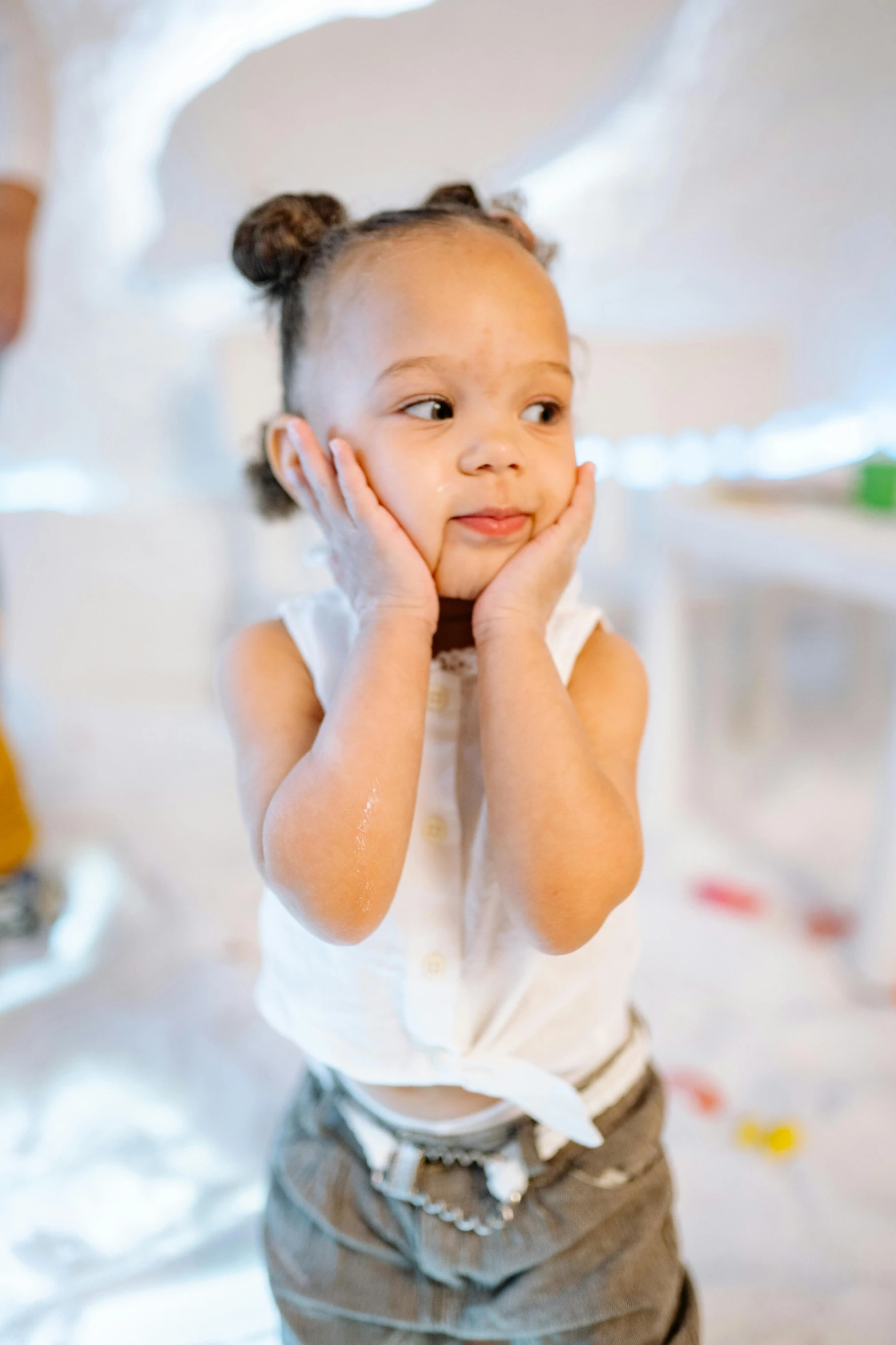 a little girl holding her hands to her face, looking to the side off camera, lights, bulky build, an all white human