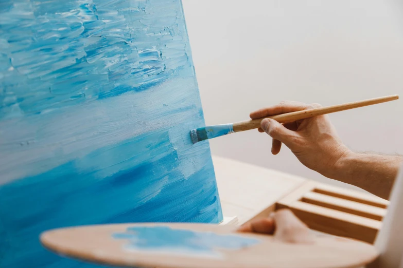 a close up of a person painting on a canvas, a photorealistic painting, inspired by Kyffin Williams, trending on pexels, blue colours, easel, minimalistic art, vibrant blue