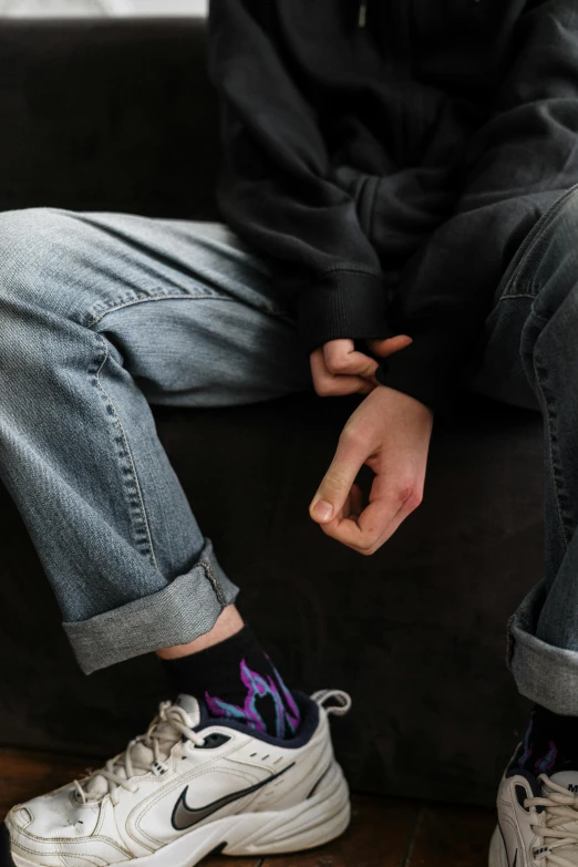 a person sitting on a couch with a pair of sneakers, trending on pexels, wearing jeans and a black hoodie, smoking and bickering, aged 13, handcuffed