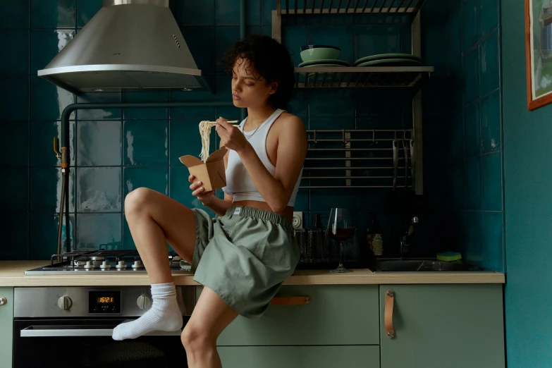 a woman sitting on top of a kitchen counter, inspired by Nan Goldin, pexels contest winner, eating noodles, bra and shorts streetwear, nathalie emmanuel, teal aesthetic