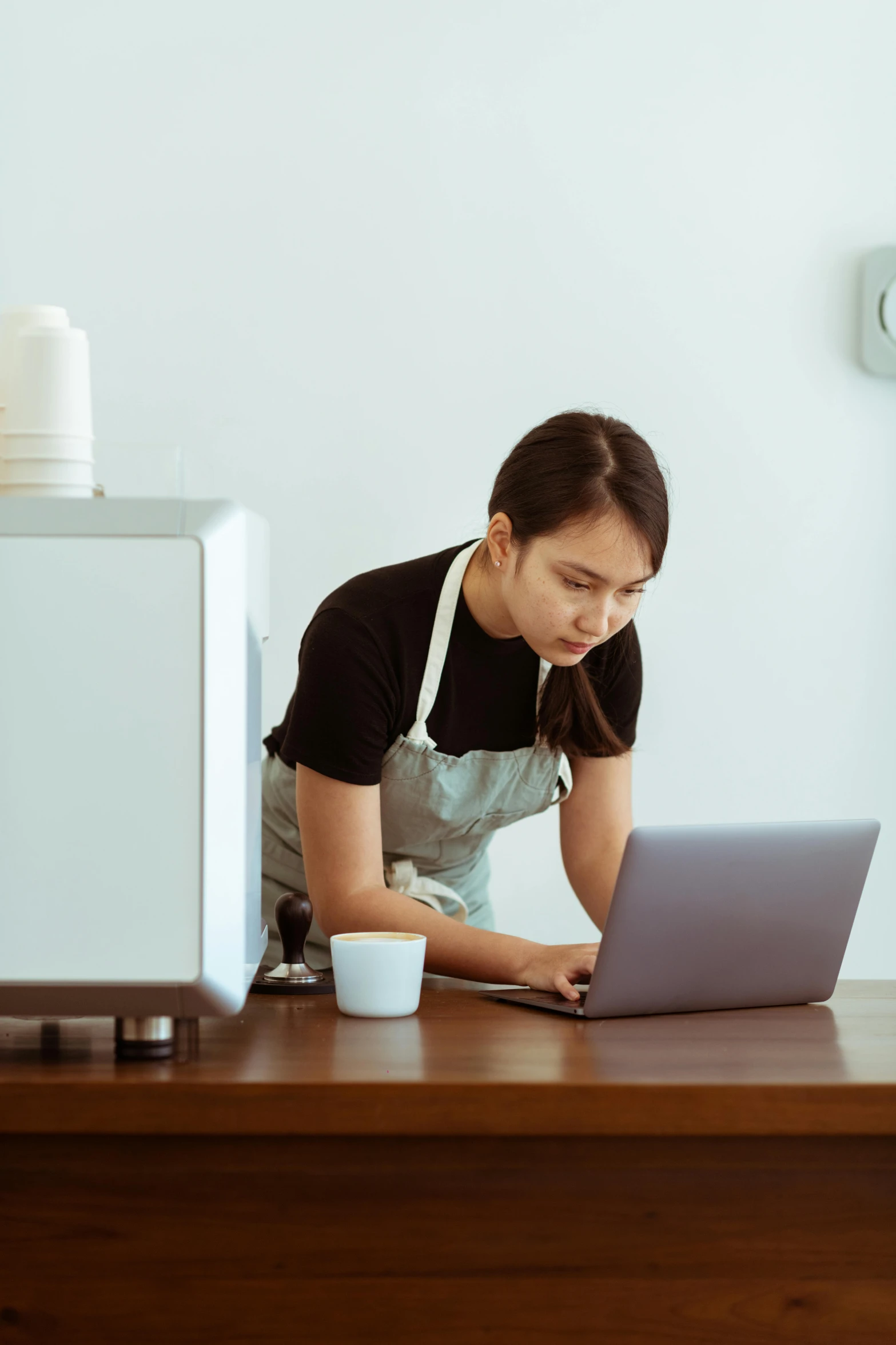 a woman in an apron working on a laptop, pexels contest winner, coffee machine, inspect in inventory image, asian female, thumbnail