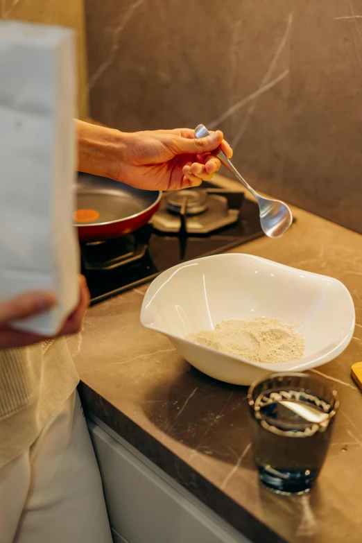 a person in a kitchen preparing food on a stove, white clay, fan favorite, spoon placed, in liquid