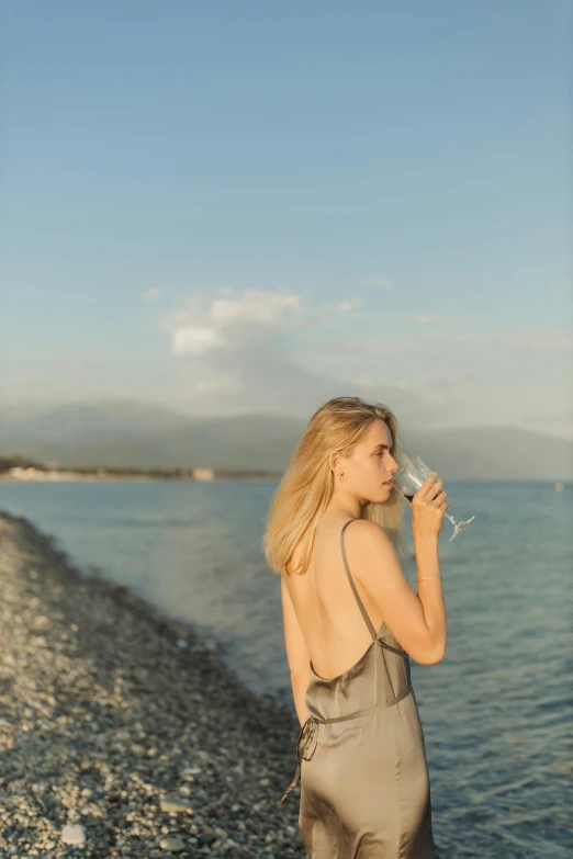 a woman standing on a beach holding a wine glass, unsplash, renaissance, medium format. soft light, young blonde woman, wearing a camisole, european woman photograph