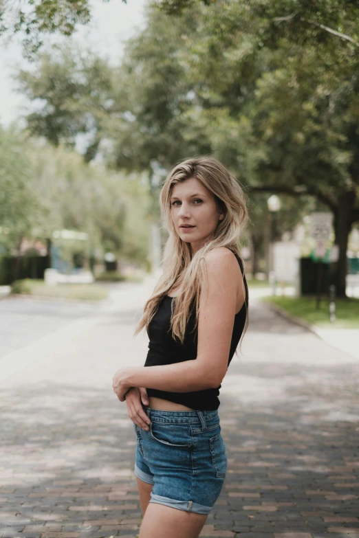 a woman standing in the middle of a street, by Kristin Nelson, with long blond hair, wearing a cropped black tank top, young southern woman, portrait featured on unsplash