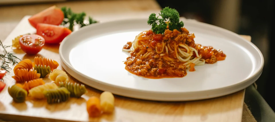 a white plate topped with pasta and vegetables, on a wooden table, 🦩🪐🐞👩🏻🦳, high quality product image”, ground meat