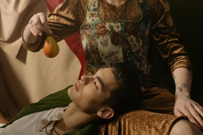 a woman sitting next to a man holding an apple, an album cover, inspired by Orazio Gentileschi, trending on pexels, renaissance, robert sheehan, movie still frame, his head is a pear, set photograph in costume
