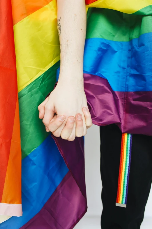 a close up of a person holding a rainbow flag, by Arabella Rankin, shutterstock, antipodeans, holding each other hands, colorful uniforms, on the cover of a magazine, couple