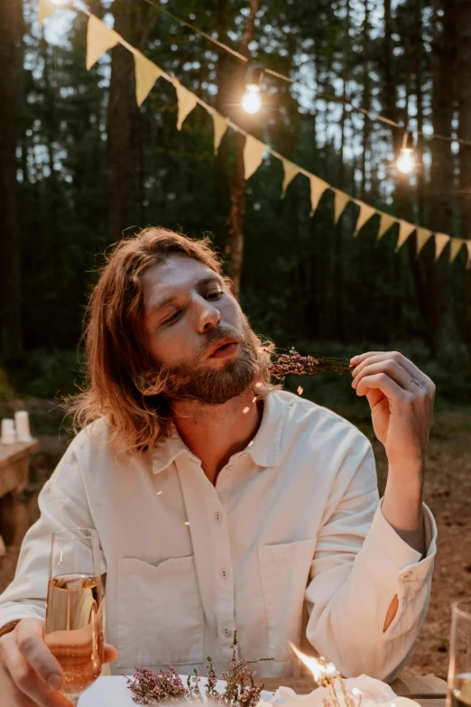 a man sitting at a table with a glass of wine, an album cover, unsplash, renaissance, evening!! in the forest, blond brown stubble thin beard, flower child, eating outside