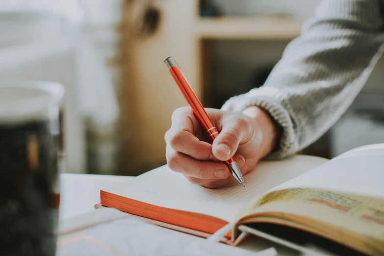 a person holding a pencil and writing on a book, light red and orange mood, school curriculum expert, multiple stories, thumbnail