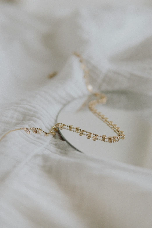 a close up of a necklace on a bed, by Nicolette Macnamara, trending on pexels, delicate detailing golden stroke, dreamy sequence, tiny details, soft vignette