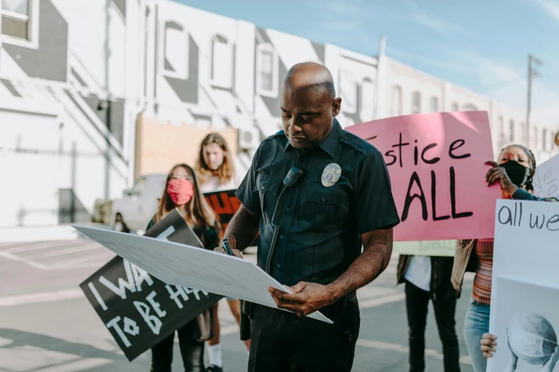 a group of people holding signs in front of a building, by Julia Pishtar, pexels contest winner, black arts movement, sad cop looking at a, holding a clipboard, wearing a police uniform, los angeles ca