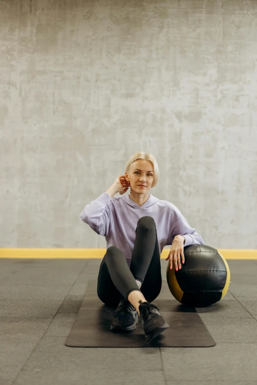 a woman sitting on a mat with a medicine ball, a portrait, by Nina Hamnett, pexels contest winner, black and yellow tracksuit, athletic crossfit build, scandinavian, dasha taran