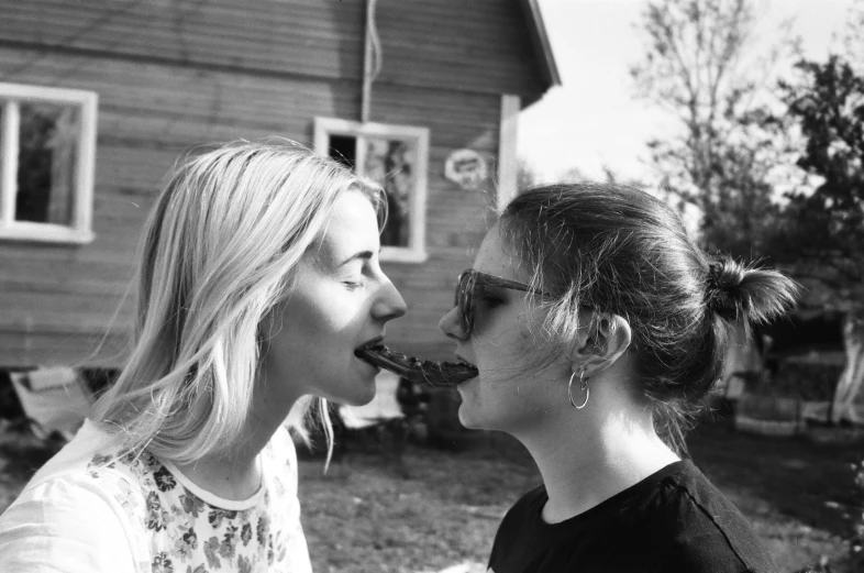 a couple of women standing next to each other, a black and white photo, by Emma Andijewska, tumblr, she is eating a peach, barbecuing chewing gum, 🌸 🌼 💮, smothered in melted chocolate