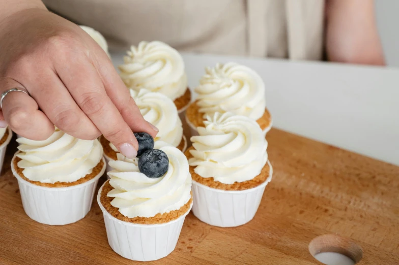 a person placing a blueberry on top of cupcakes, by Niko Henrichon, trending on unsplash, figuration libre, white, cream, official product photo, rectangular