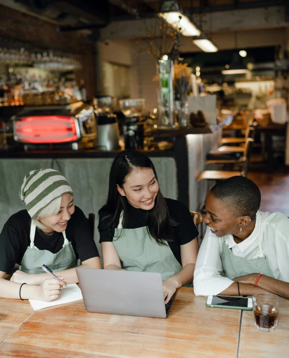 a group of people sitting at a table with a laptop, wearing an apron, unsplash transparent, lesbian, asian descent