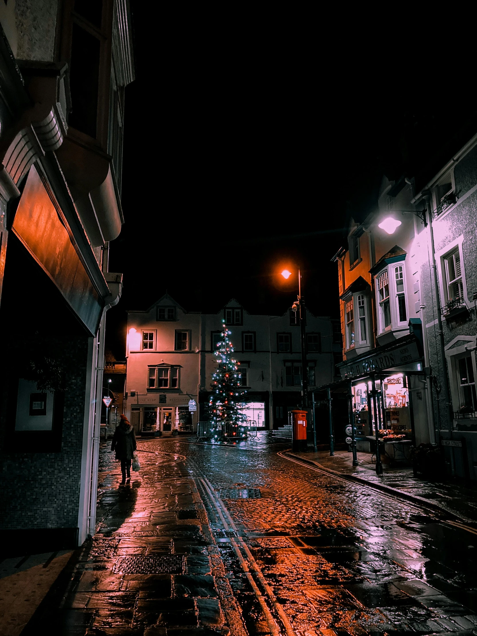 a person walking down a wet street at night, an album cover, by IAN SPRIGGS, pexels contest winner, christmas night, town square, 💋 💄 👠 👗, wales