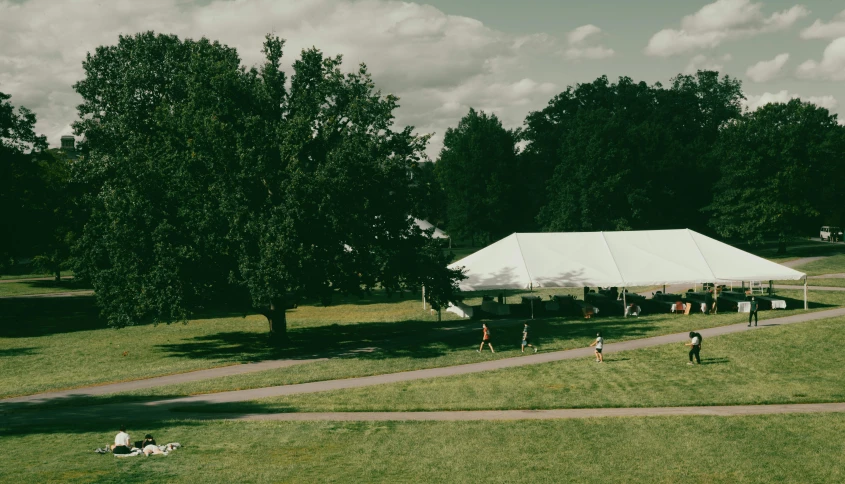 a large white tent sitting on top of a lush green field, unsplash, people walking around, college, 1990's photo