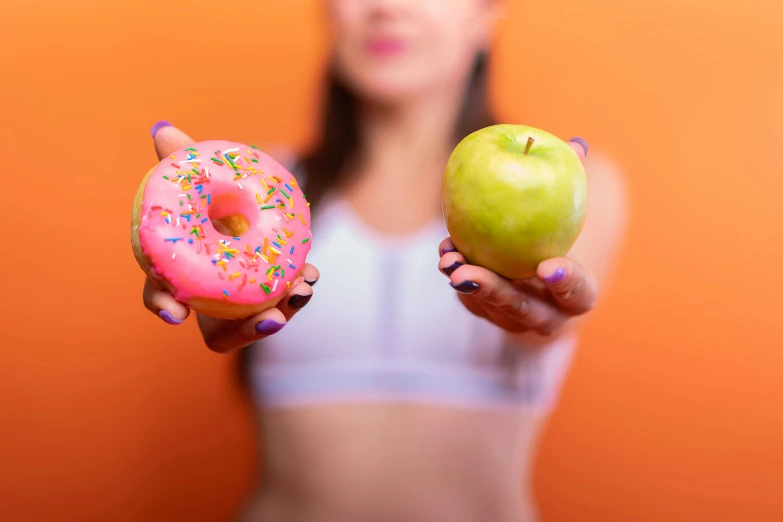 a woman holding two donuts and an apple, pexels, fit physique, pink and orange, 🦩🪐🐞👩🏻🦳, complementary colours